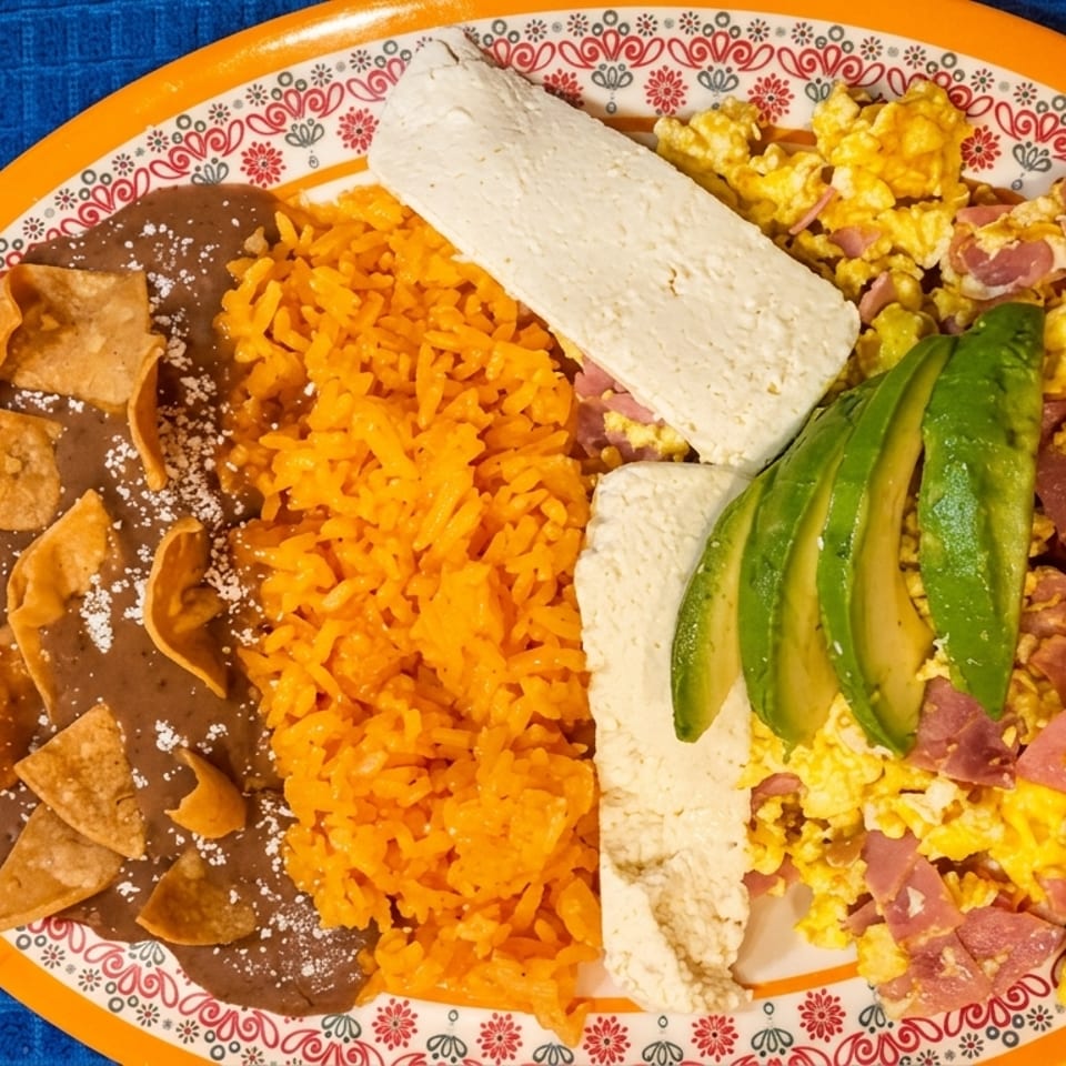 Mexican breakfast plate with refried beans, rice, scrambled eggs with ham, cheese, and avocado slices.